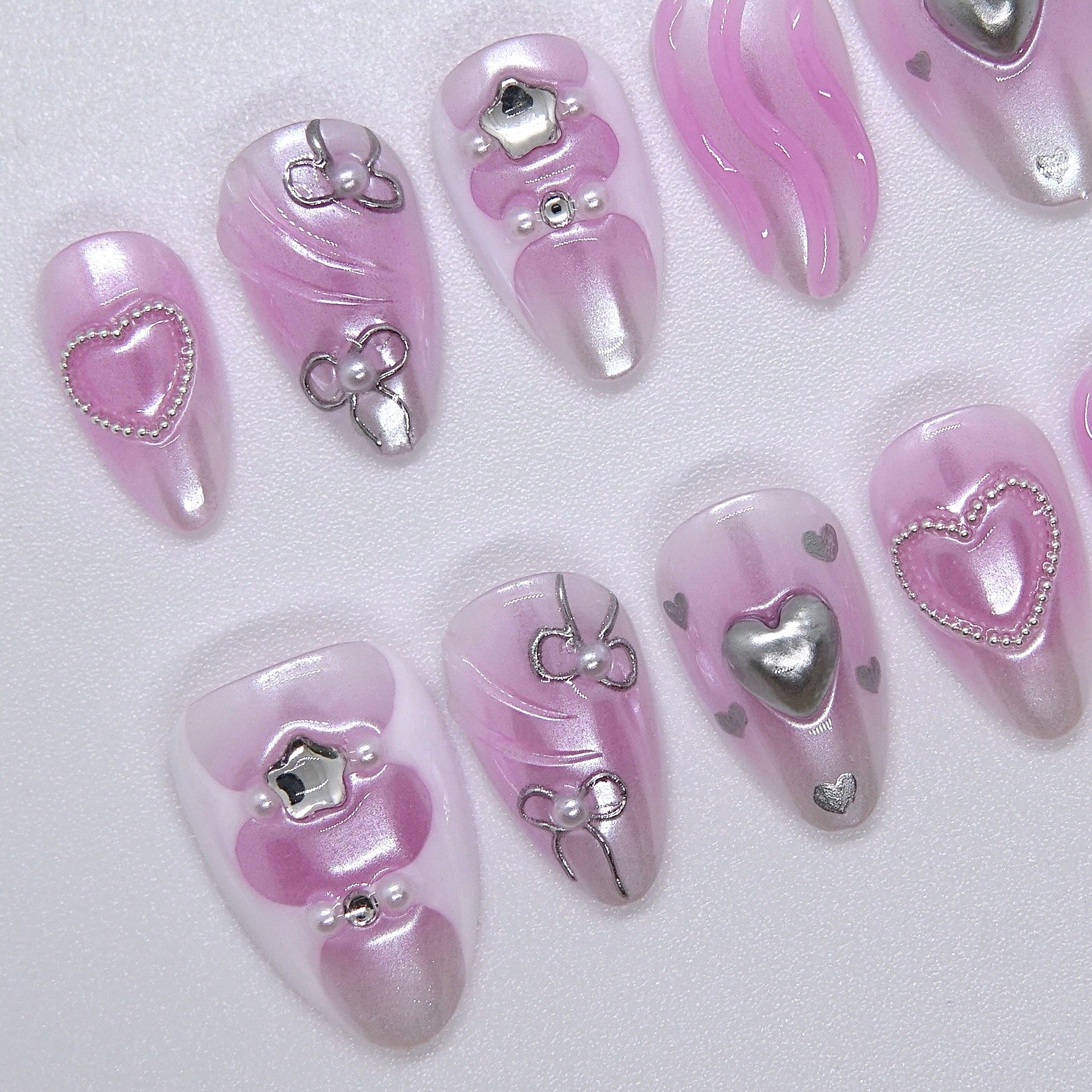 Side angle of handcrafted pink press-on nails featuring silver swirl and heart motifs
